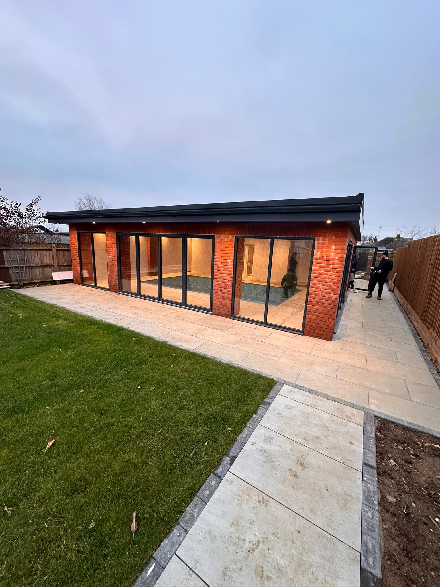 Glazed pool space beside a landscaped Northampton garden at dusk